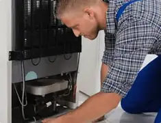 Refrigerator repair technician servicing the compressor and condenser area in Fort Worth, TX
